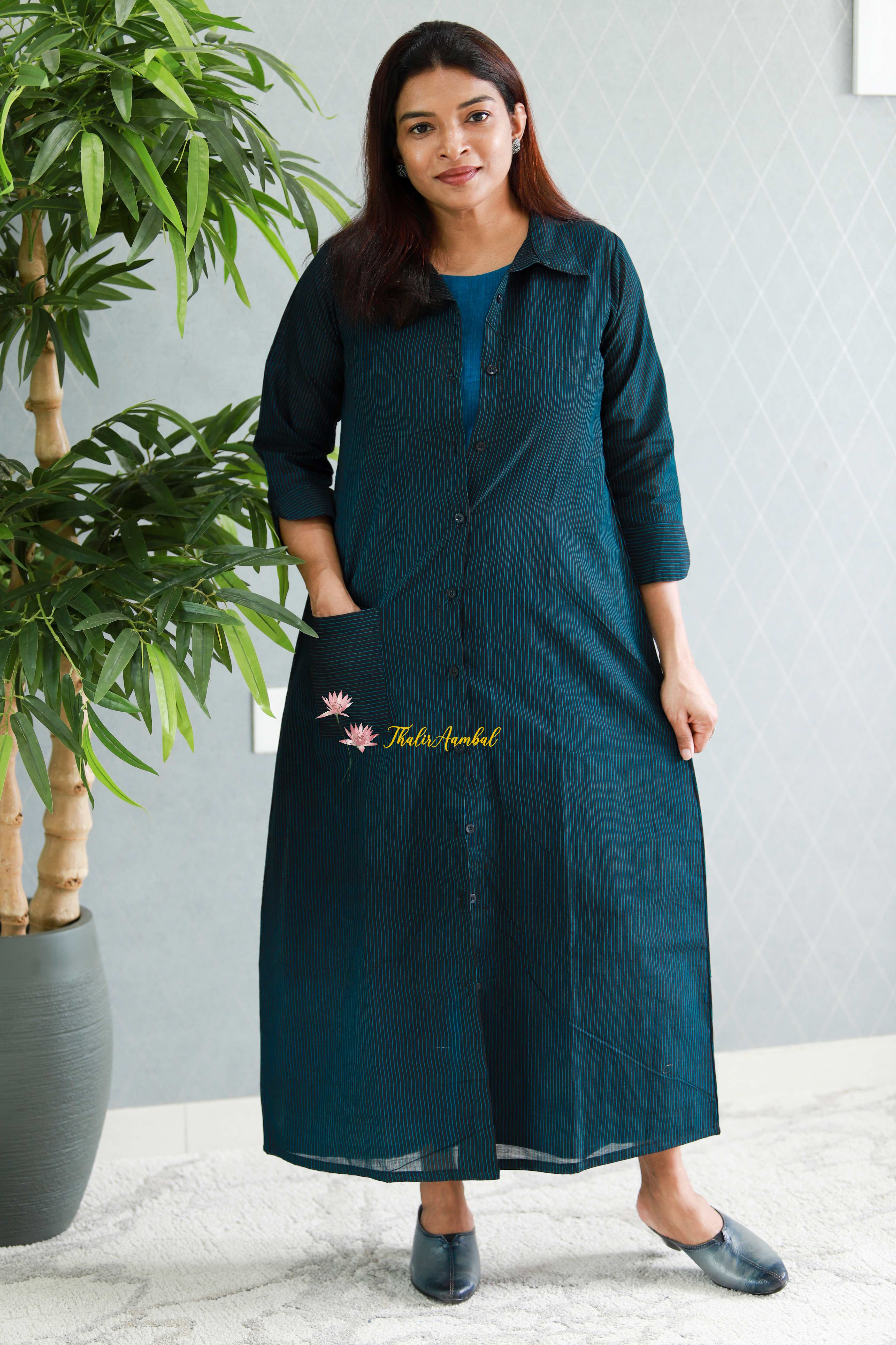 Woman wearing a teal black dress standing indoors with a plant in the background. Thaliraambal
