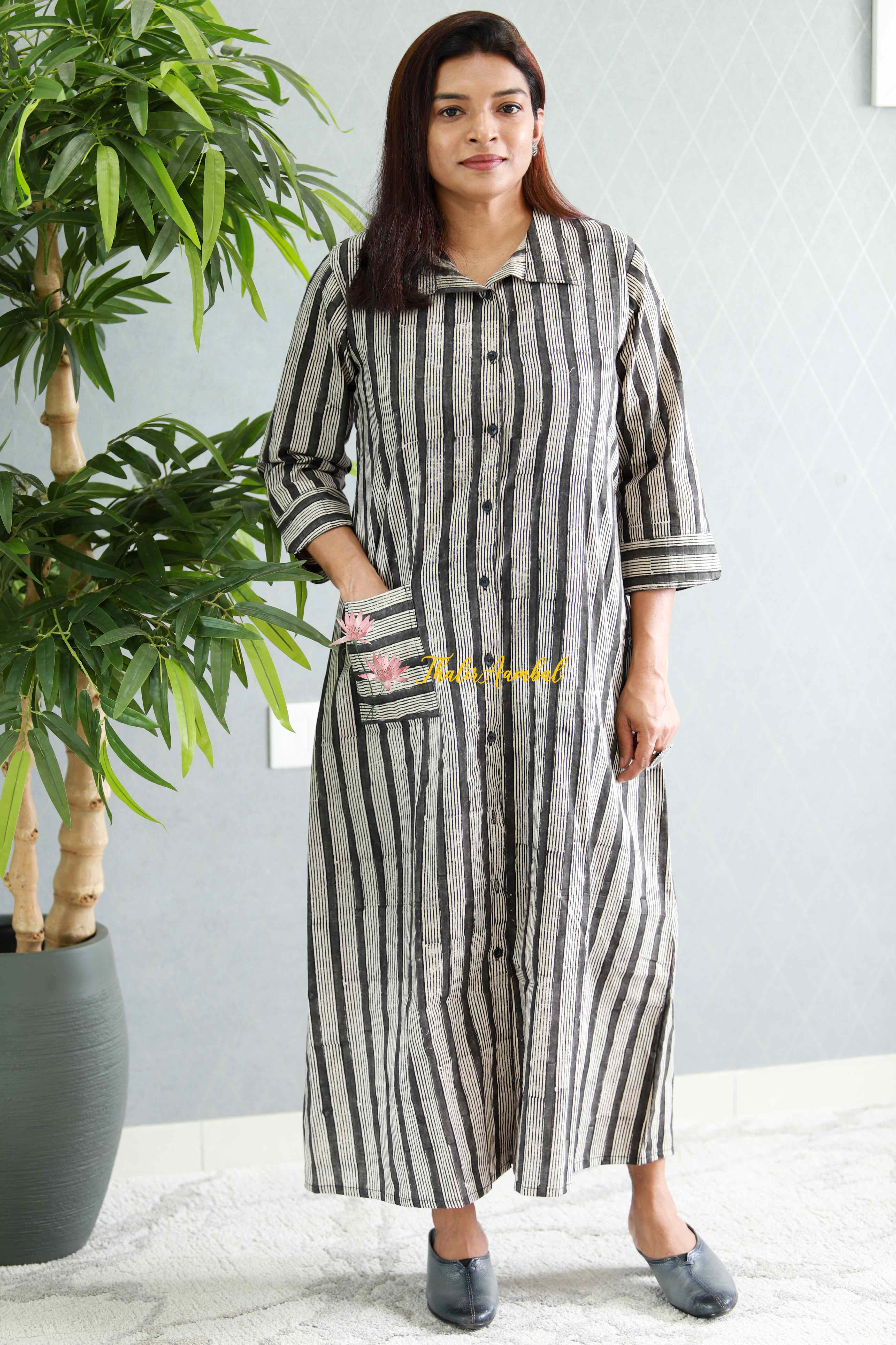 Woman wearing a black and white striped dress standing next to a potted plant indoors.Thaliraambal
