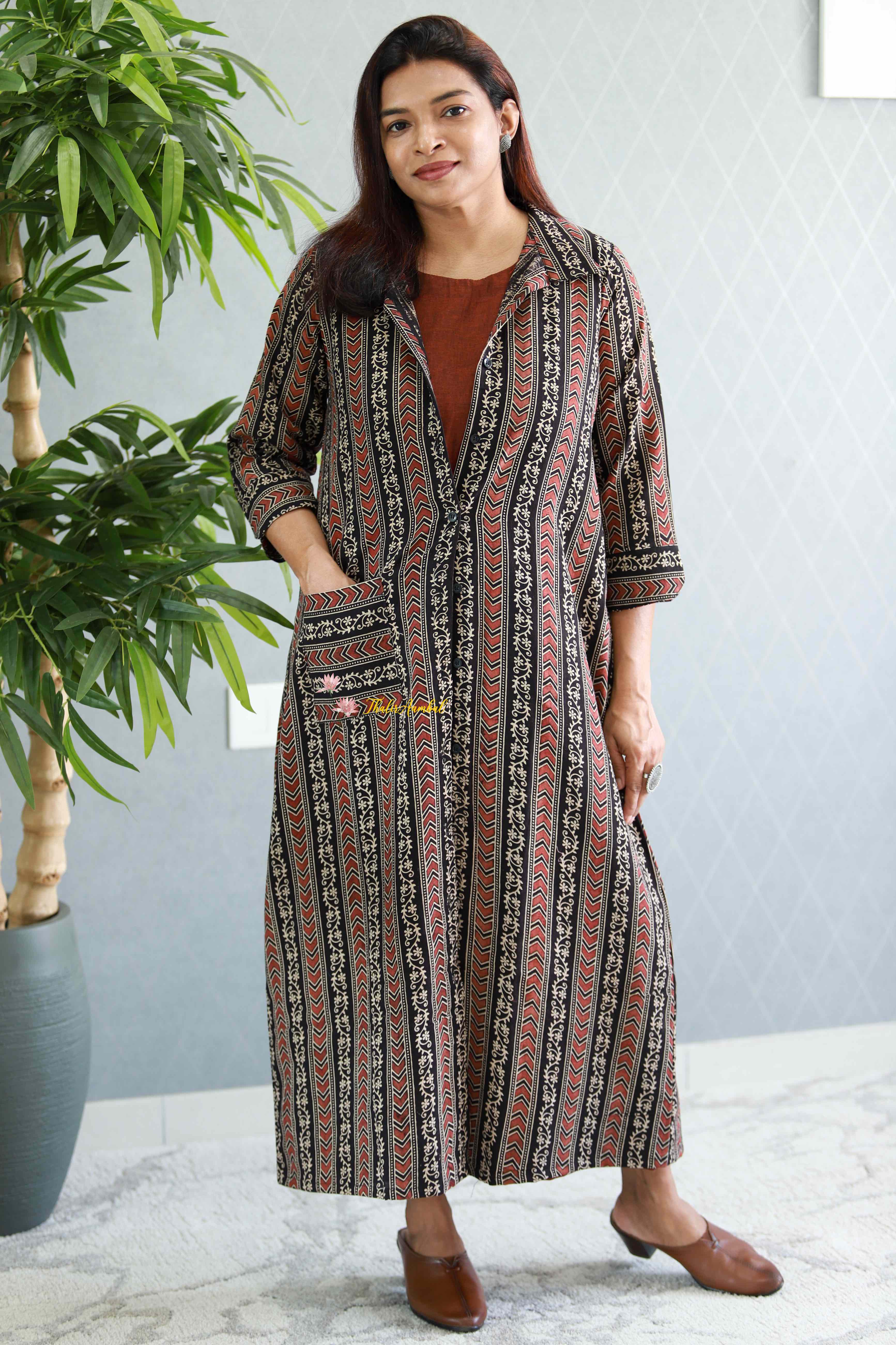 Woman wearing a patterned dress standing indoors with a plant in the background