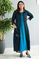 Woman wearing a long black and blue dress standing indoors with a plant in the background .Thaliraambal