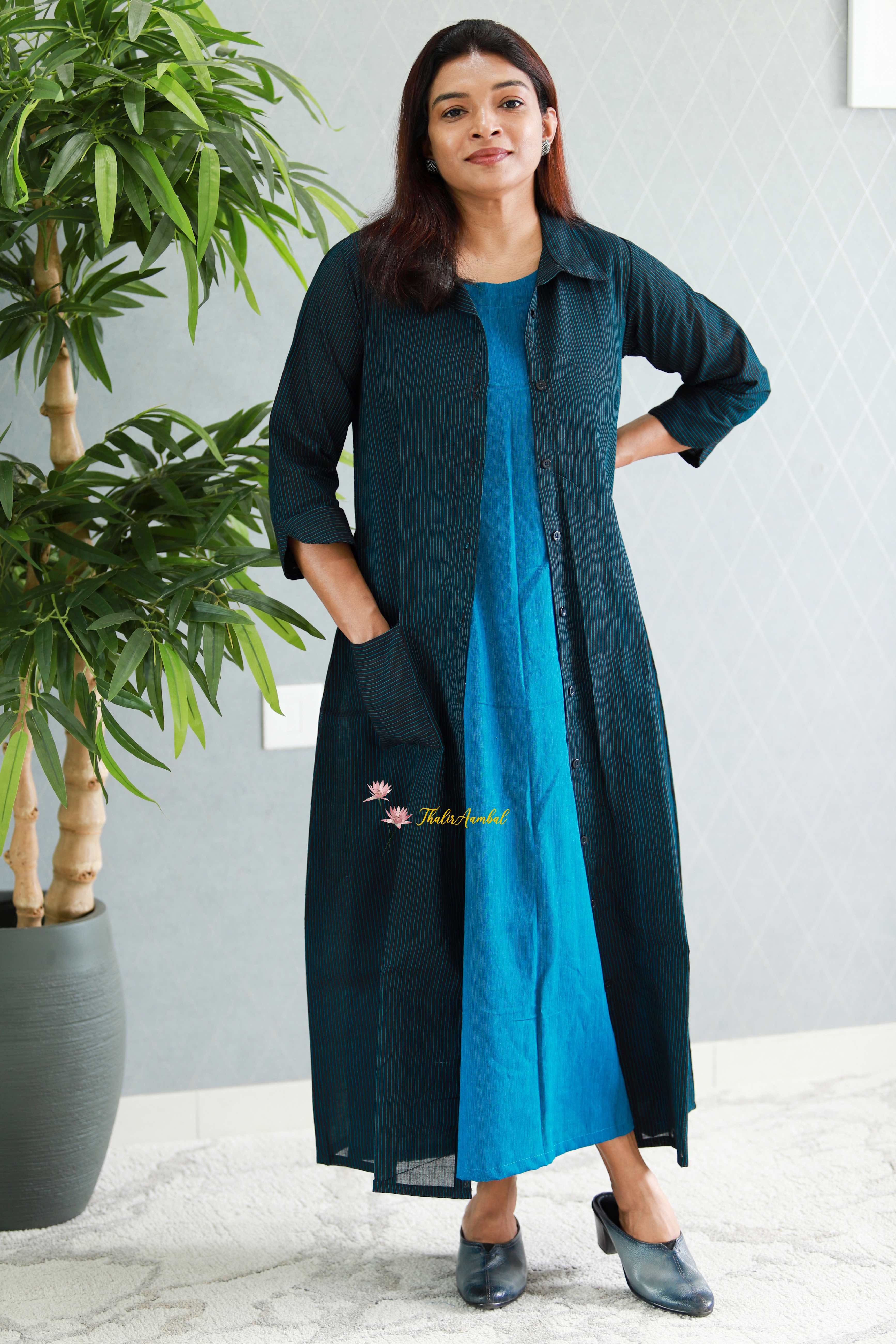 Woman wearing a long black and blue dress standing indoors with a plant in the background .Thaliraambal