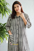 Woman wearing a black and white striped shirt with a plant in the background.Thaliraambal