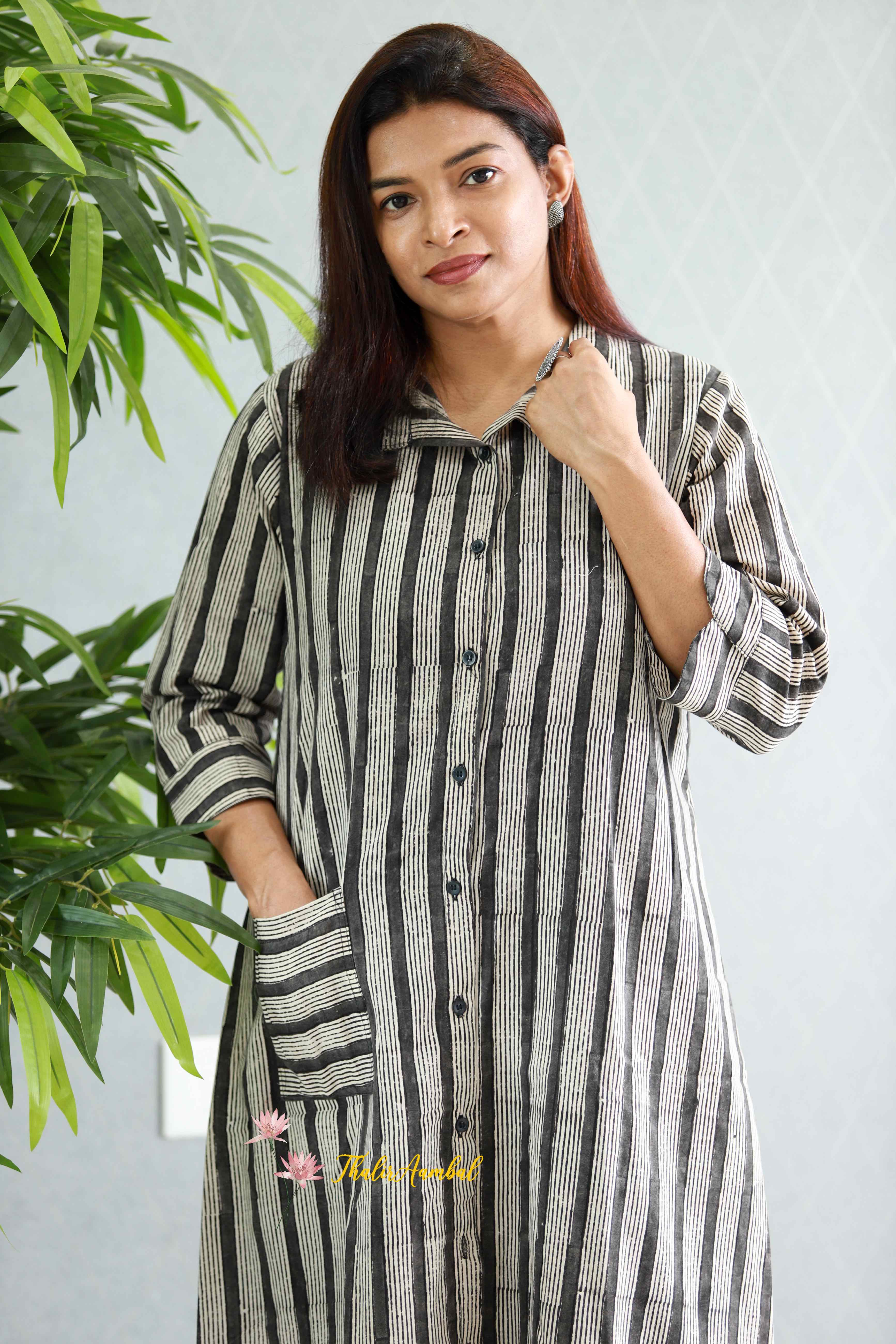 Woman wearing a black and white striped shirt with a plant in the background.Thaliraambal