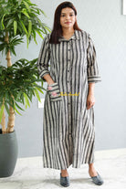 Woman wearing a black and white striped dress standing next to a potted plant indoors.Thaliraambal