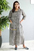 Woman wearing a long black and white striped dress standing indoors with a plant in the background.Thaliraambal