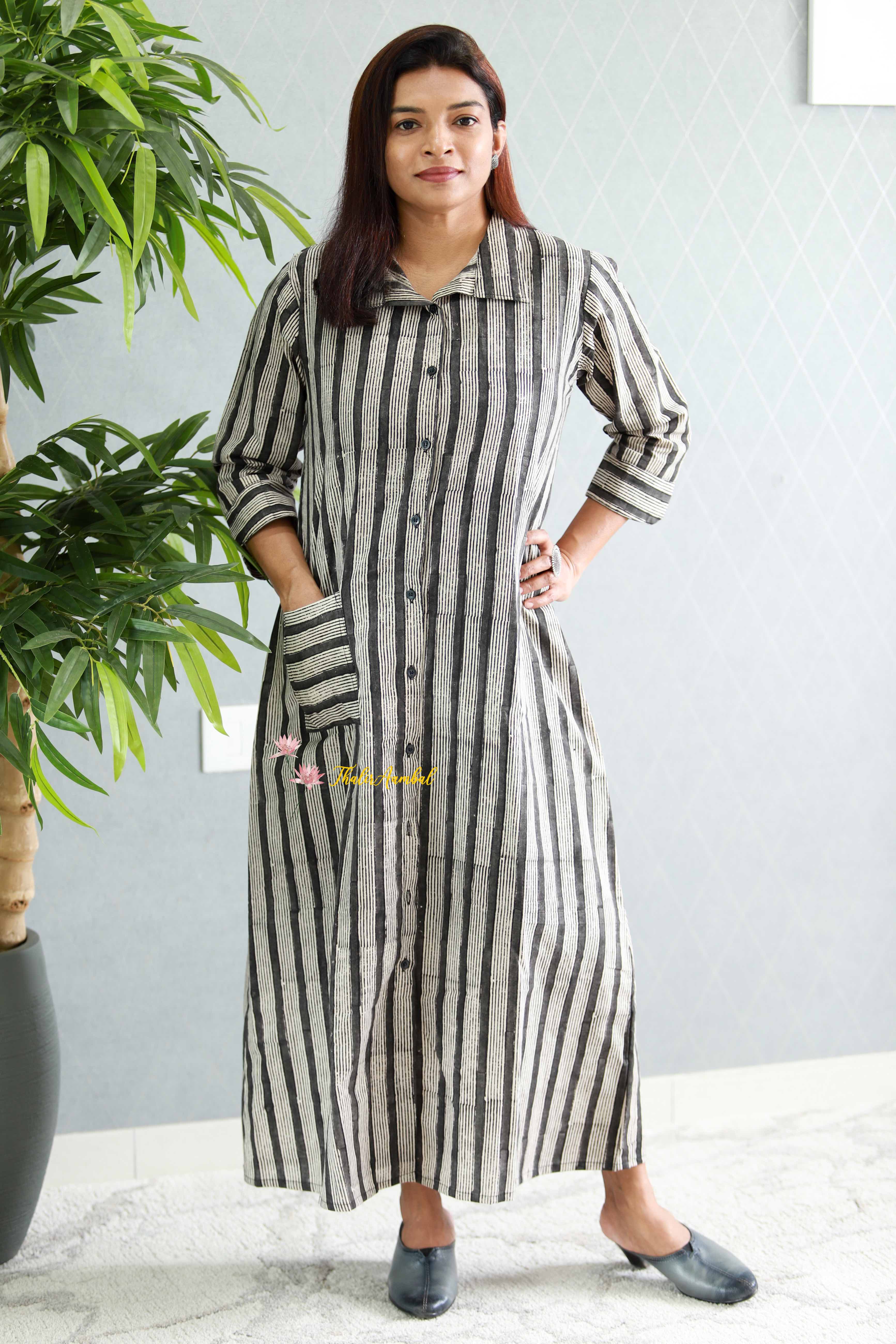 Woman wearing a long black and white striped dress standing indoors with a plant in the background.Thaliraambal