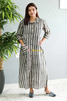 Woman wearing a long striped dress standing indoors with a plant in the background.Thaliraambal