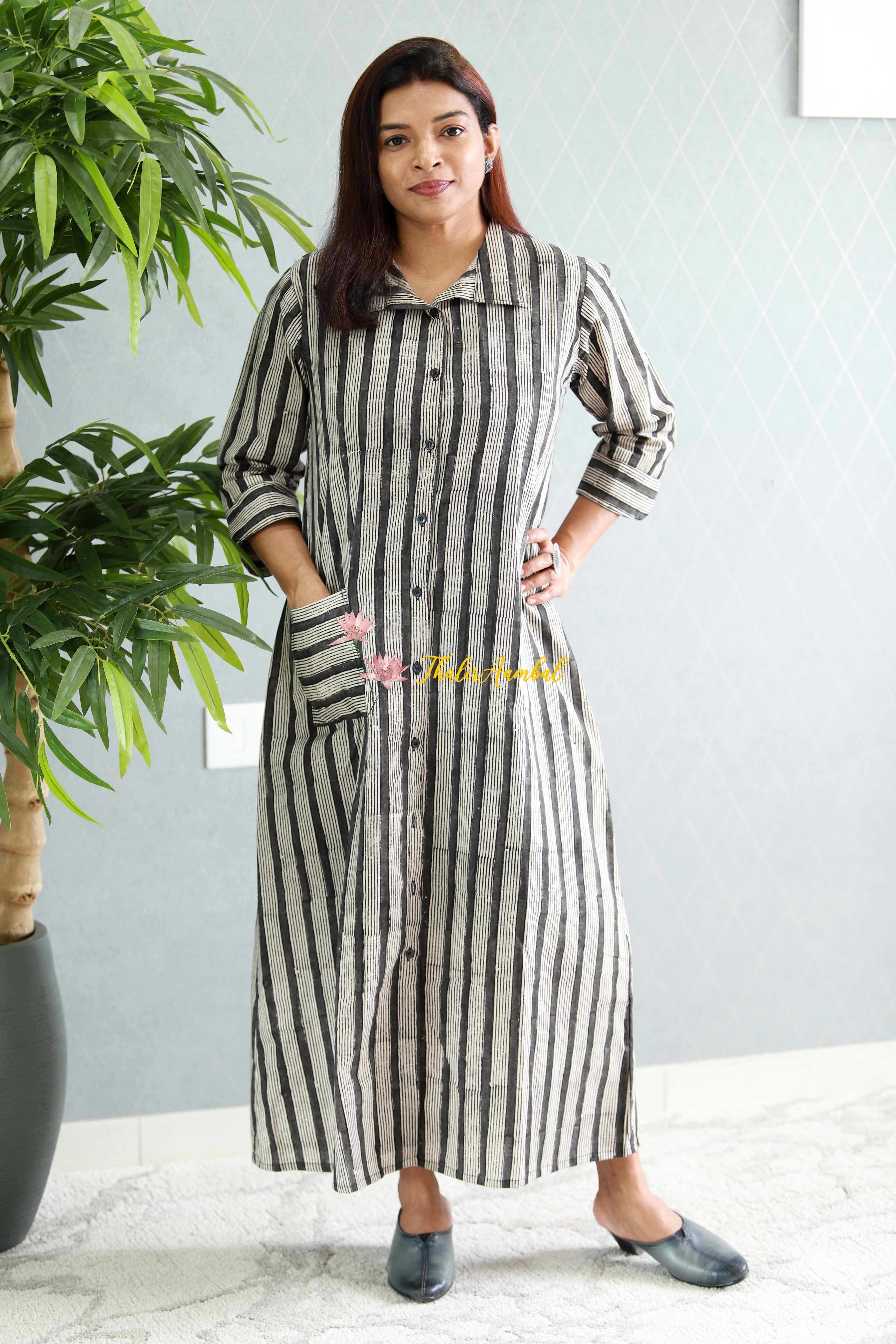 Woman wearing a long striped dress standing indoors with a plant in the background.Thaliraambal