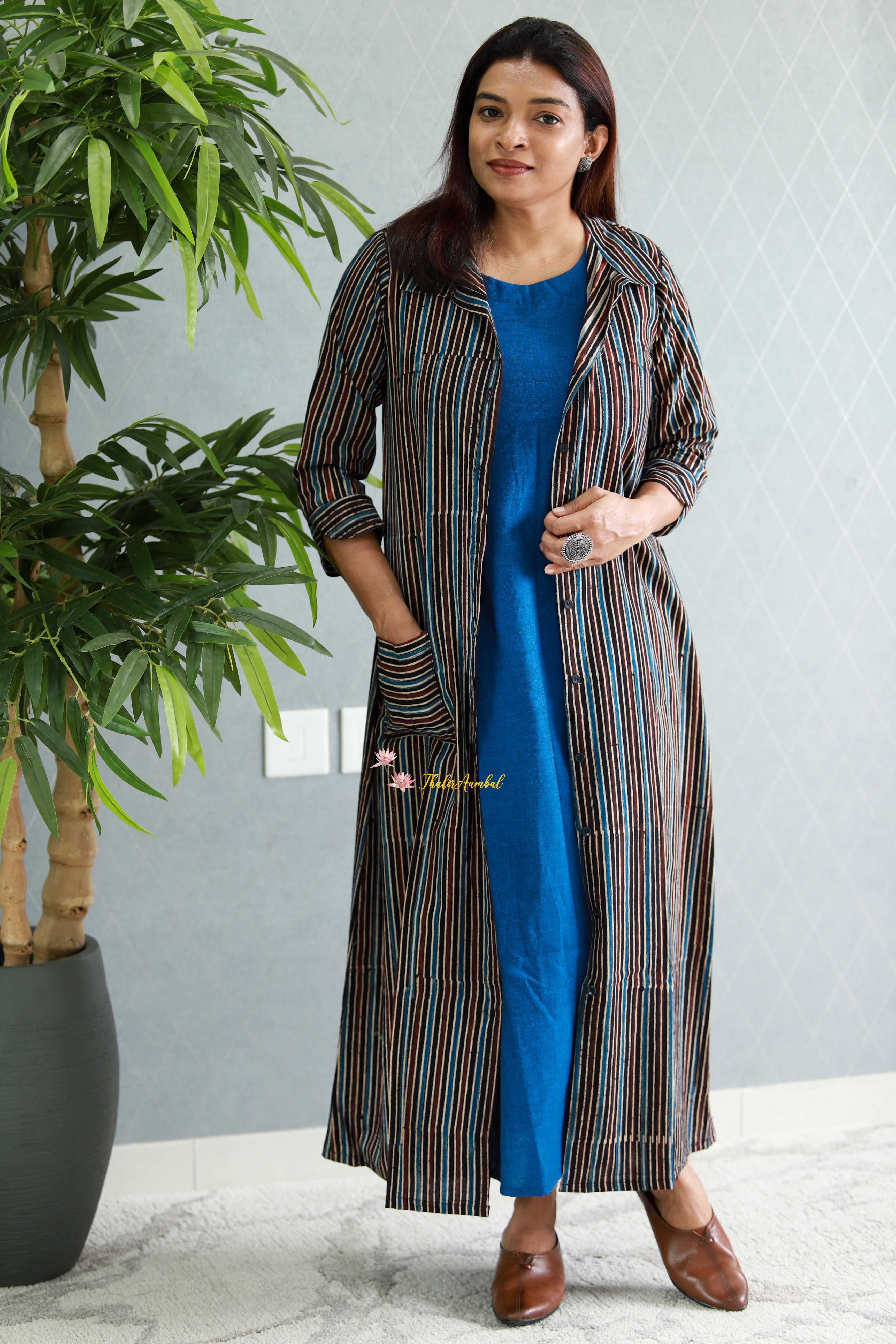 Woman wearing a blue dress with a long striped coat in a room with a plant.-Thaliraambal