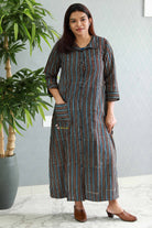 Woman wearing a striped dress standing indoors with a plant in the background.Thaliraambal