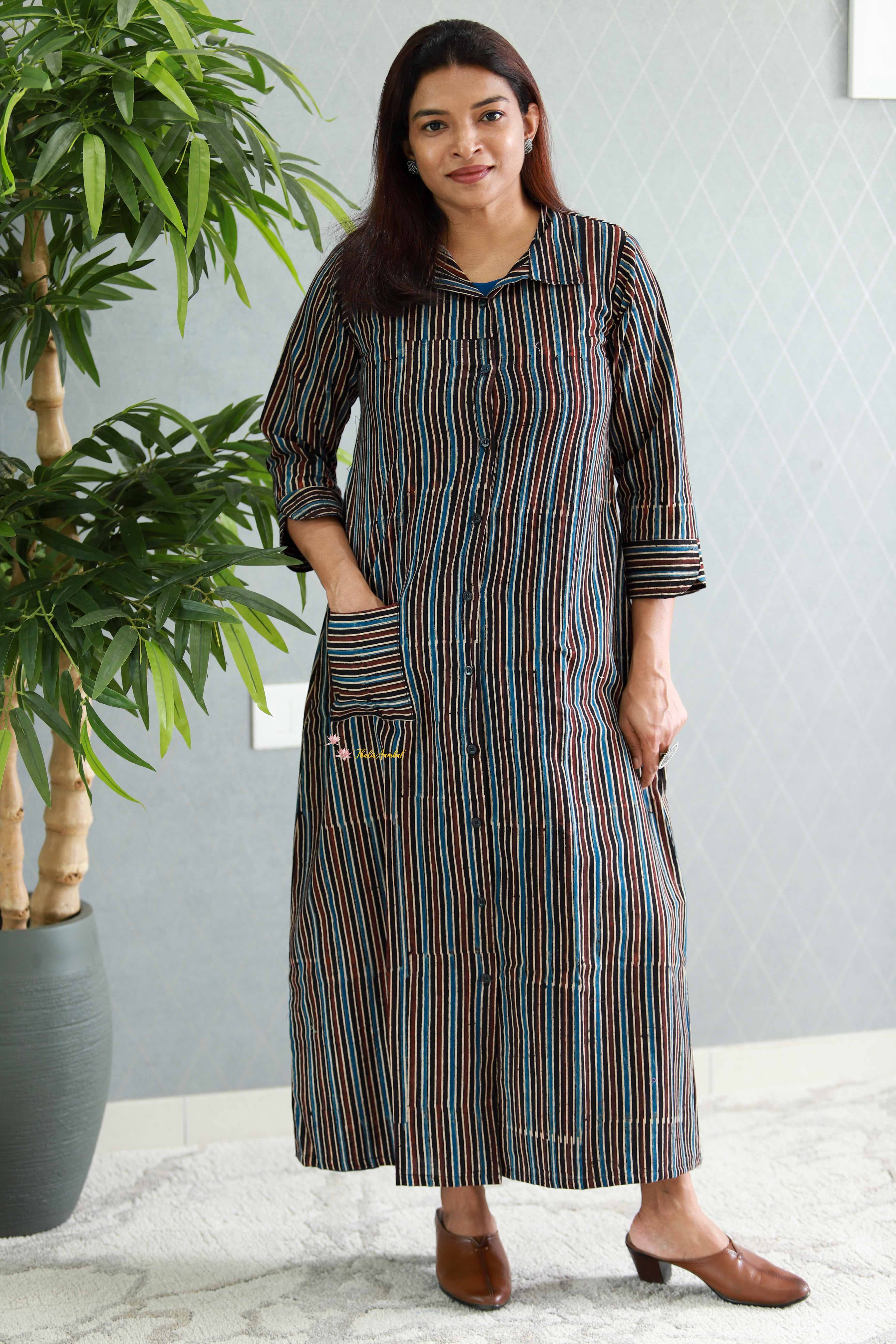 Woman wearing a striped dress standing indoors with a plant in the background.Thaliraambal