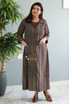 Woman wearing a patterned dress standing next to a potted plant indoors.Thaliraambal