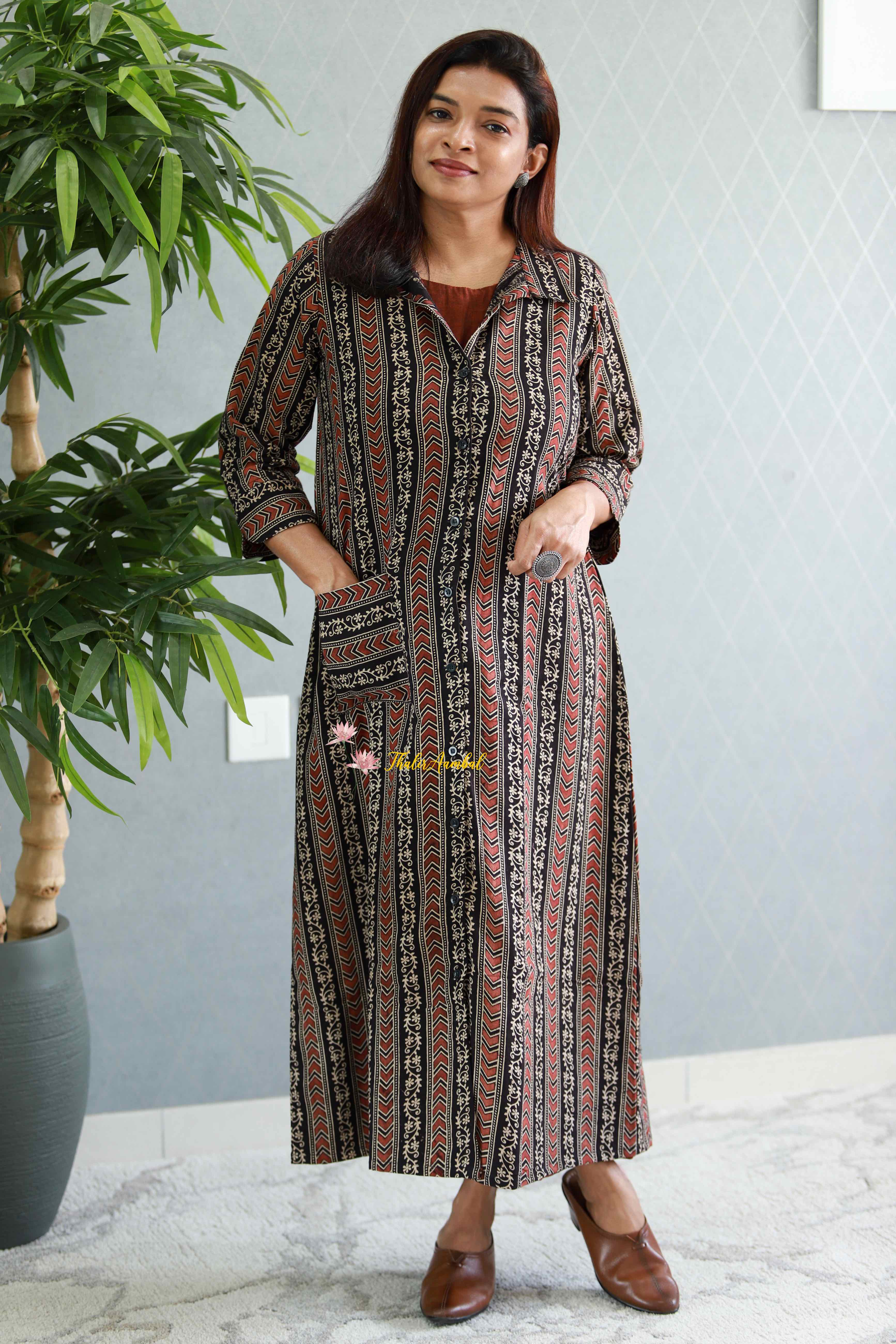 Woman wearing a patterned dress standing next to a potted plant indoors.Thaliraambal