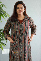 Woman wearing a patterned long dress with a neutral background.Thaliraambal