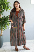 Woman wearing a patterned dress standing indoors with a plant in the background