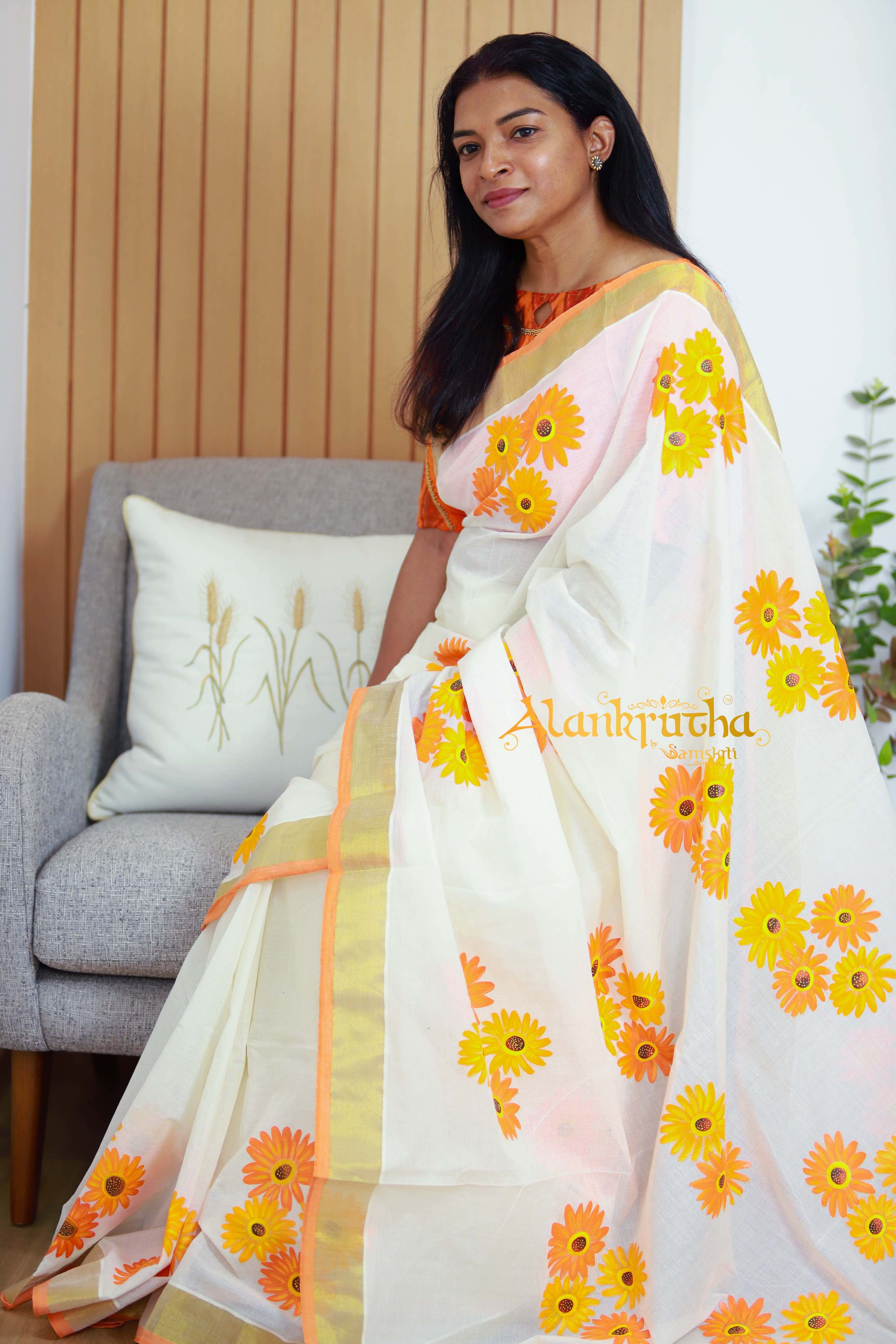 Woman wearing a floral saree with a visible brand name, sitting on a couch. Thaliraambal