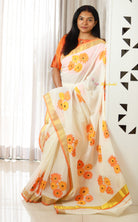 Woman wearing a floral saree with an orange and yellow pattern against a white curtain background.Thaliraambal